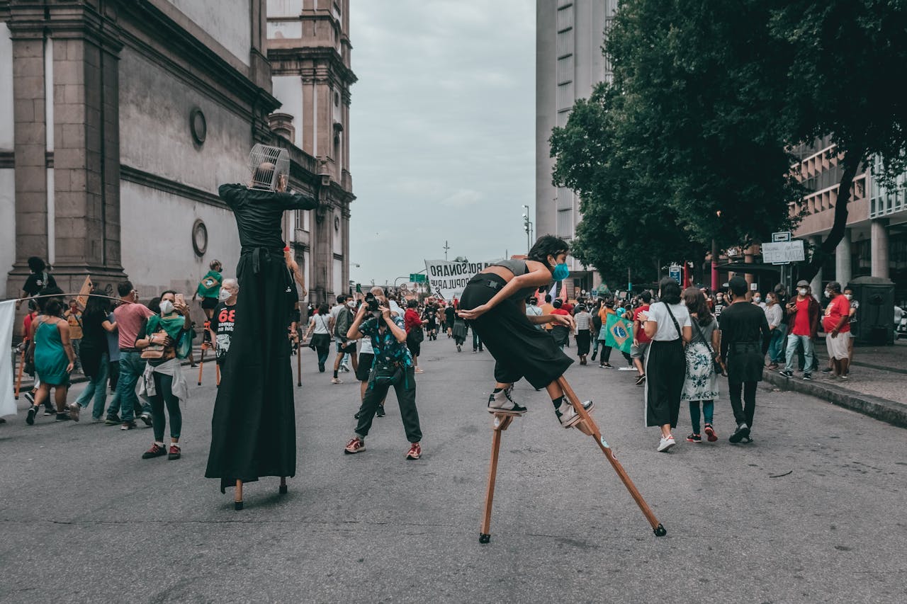 A vibrant street protest in Rio de Janeiro with performers on stilts engaging the crowd.